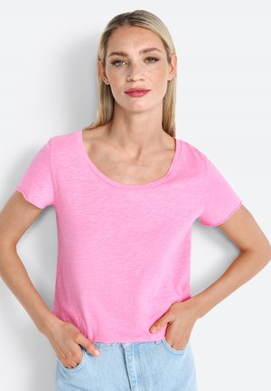 T-shirt rose à manches courtes avec un col arrondi, fabriqué dans un tissu léger et doux. Coupe décontractée, porté avec les mains dans les poches d'un jean bleu clair.