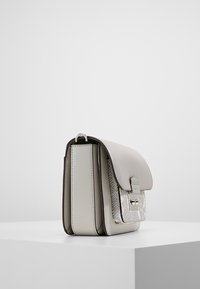 Světle šedá kabelka s hladkým koženým povrchem, s texturovaným akcentem v hadím vzoru a klopovým uzávěrem s kovovými detaily.