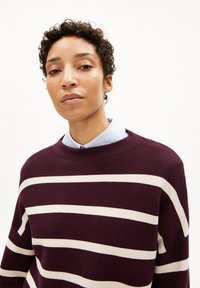 Bordeaux-roter Strickpullover mit breiten horizontalen cremefarbenen Streifen, Rundhalsausschnitt und lockerer Passform. Glatte Textur, minimalistisches Design und lässiger Stil.