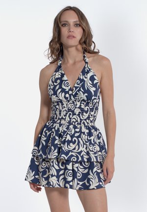 Robe halter bleu marine avec un motif floral blanc, dotée d'un corsage smocké ajusté et d'une jupe à volants superposés. Le tissu a une texture lisse.