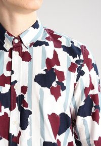 Overhemd met knopen in een witte basis met een kleurrijk abstract patroon van rode, marineblauwe en blauwe penseelstreken; met kraag en witte knopen.