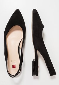 Zapato de tacón slingback de ante negro con punta afilada, tacón bajo y detalle recortado en los laterales. Contiene una plantilla suave de color beige con marca.