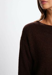 Maglione lavorato a maglia marrone con un design a coste texturizzate. Presenta un ampio scollo e spalle scese, sottolineando un fit rilassato.