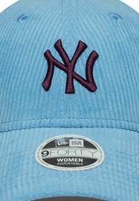 Căciulă de baseball din catifea ușor albastră, cu un logo brodat de culoare purpurie al New York-ului și un autocolant rotund de ajustare a mărimii pe vizieră.