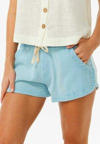 Himmelblaue Shorts mit einem Kordelzugbund, seitlichen Taschen und einer weichen Textur, kombiniert mit einem weißen Button-Up-Oberteil und Holzknöpfen.