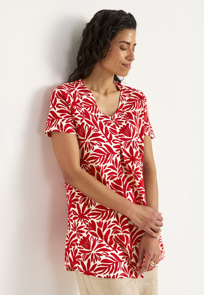 Rød og creme kortærmet top med et blomstret bladmønster, v-hals og afslappet pasform. Stoffet virker let og blødt.