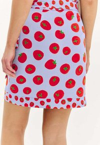 Modrá sukňa pokrytá červenými vzormi paradajok so zelenými stonkami. Dizajn obsahuje lem s menšími tlačenými paradajkami. Hladká textura tkaniny.
