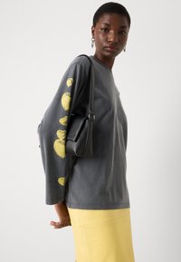 Gray long-sleeve t-shirt featuring yellow heart prints on the left sleeve, paired with a yellow skirt and a small black handbag.