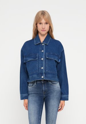 Jachetă din denim albastru, croită, cu închiderea prin butoane, două buzunare pe piept și mâneci lungi. Materialul are o textură distinctivă și cusături contrastante.