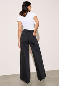 Magas derekú, fekete vászon nadrág, széles lábakkal, hátoldali zsebekkel és letisztult kivitelezéssel. Az anyag strapabíró és textúrált hatású.