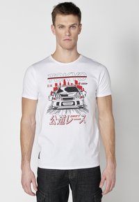 Tricou alb din bumbac, cu un design grafic al unei mașini, însoțit de textul "TOKYO" și "DRIFT" scris cu litere roșii. Mâneci scurte și guler rotund.