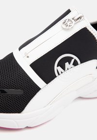 Svart och vit sportskor med nätframsida, sidodragkedja med rund dragkedja och silverfärgad MK-logotyp på sidopanelen.