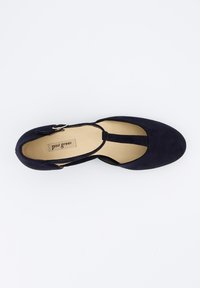 Zapato plano de ante azul marino con puntera redondeada, tira al tobillo y pequeña hebilla dorada. El interior cuenta con un forro beige con la etiqueta de la marca.