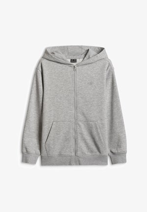 Enfant debout portant un sweat à capuche gris zippé, un pantalon de jogging assorti, des baskets noires et blanches, des chaussettes blanches et un bonnet en tricot bleu.