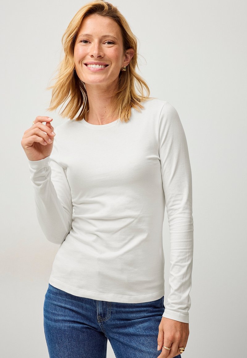 Witte longsleeve T-shirt van zachte stof, met een ronde halslijn en een getailleerd ontwerp, gecombineerd met een blauwe jeans.
