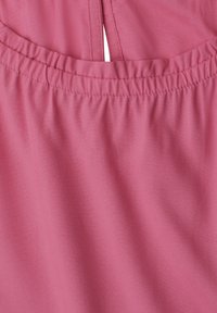 Close-up of pink fabric with gathered elastic stitching and a centered vertical seam detail at the top edge.