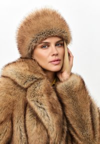Cappotto di pelliccia marrone con pelliccia spessa e strutturata e un cappello di pelliccia abbinato. Presenta un gradiente di colore naturale e linee eleganti sul capo.