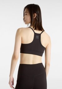 Schwarzer Sport-BH mit Racerback-Design und Logodetail. Verfügt über eine nahtlose Textur und Flachnahtnähte für zusätzlichen Komfort.