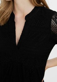 Svart spetsklänning med V-ringning, korta ärmar och texturerade mönster över hela tyget, med en utsvängd midja.