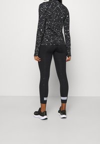 Schwarzes sportliches Langarmoberteil und Leggings mit weißen geometrischen Mustern, ausgestattet mit einem figurnahen Schnitt und kontrastierenden Taillendetails.