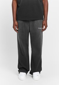 Grey sweatpants in a relaxed fit, featuring a smooth texture and embroidered "RETERNITY" logo on the left thigh. Paired with white sneakers.