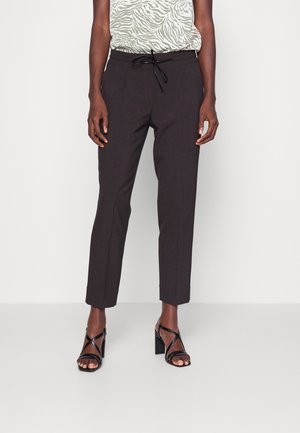 Pantalons noir ajustés avec une taille à cordon, coupe fuselée, texture subtile et poches avant. Portés avec un haut à motif vert et des sandales à talons noires.