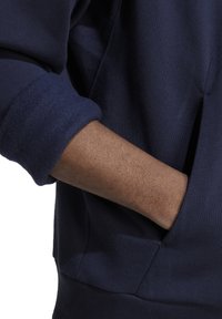 Felpa navy con polsini piegati, tessuto morbido e tasca laterale dal design elegante, che mette in risalto una vestibilità rilassata e una texture comoda.
