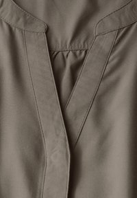 Beige Bluse mit V-Ausschnitt, plissiertem Detail und glatter Stofftextur mit feiner Naht entlang der Kanten.