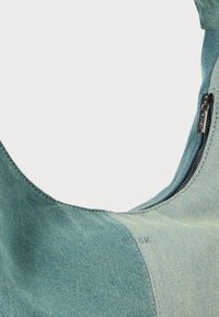 Blå denim axelväska med en slät yta, böjd design, kontrasterande grön panel och en dragkedjestängning på ena sidan.