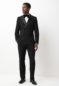 Black tuxedo with satin lapels, white dress shirt, and black bow tie. Tailored fit with double-breasted design and black leather shoes.