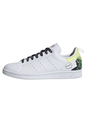 Biały sneaker Adidas z czarnymi sznurówkami, perforowanymi bocznymi paskami i zieloną kartonową twarzą z dymkiem na pięcie.
