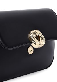 Borsa a mano in pelle nera con chiusura in metallo dorato a nodo attorcigliato e bottone a pressione, bordi curvi e texture liscia.