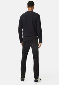 Zwart katoenen sweatshirt en donkerdenim jeans gedragen met witte en marineblauwe sneakers. De jeans hebben een standaard pasvorm en klassieke zakken.