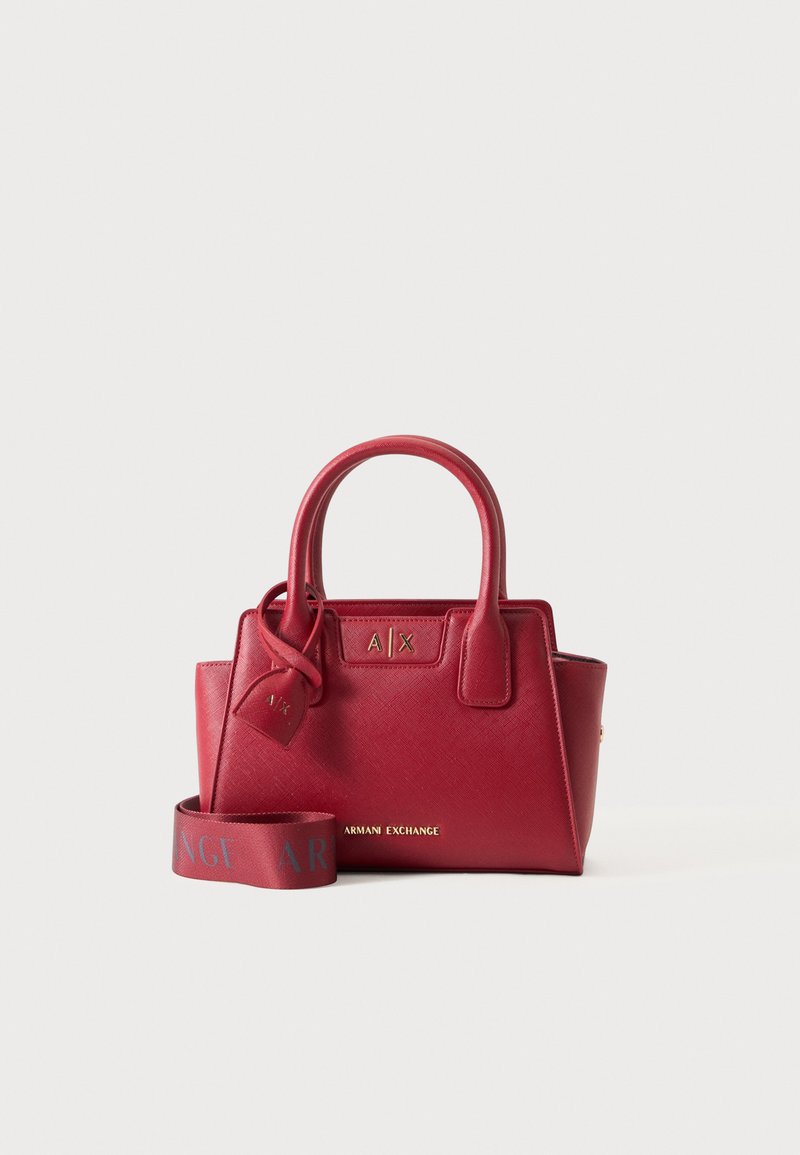Κόκκινη δερμάτινη τσάντα Armani Exchange με επάνω χερούλια, αποσπώμενο ιμάντα με λογότυπο και χρυσό λογότυπο μπροστά σε μονόχρωμο φόντο.