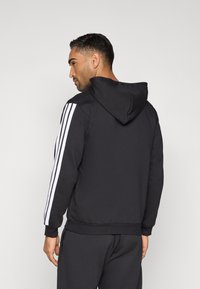 Čierna mikina s kapucňou z bavlneného blendu, so sťahovacou kapucňou a kontrastnými bielymi pruhmi pozdĺž rukávov. Hladká textúra, štandardný strih.