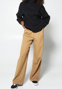 Svart ribbade polotröja, beiga vida byxor, svart och vit sneakers. Slät tyg, avslappnad passform och klassiska designfunktioner.