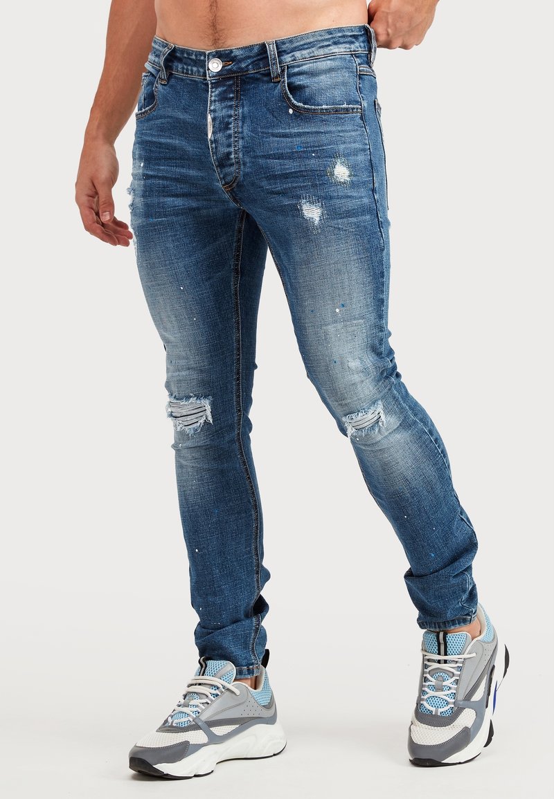 Jeans av denim i medelblå färg med slitna detaljer, urblekta områden och rivna knän. Har en klassisk femficksdesign och knappstängning.