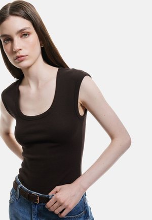 Top marrone a coste senza maniche con scollatura ampia, abbinato a pantaloni corti in denim a vita alta e una cintura marrone con accessori dorati.
