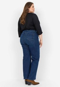 Tumši zili džinsi ar augstu vidukli, taisnu kāju dizainu un divām aizmugures kabatām. Valkāti ar melnu augšdaļu un brūniem augstpapēžu zābakiem.