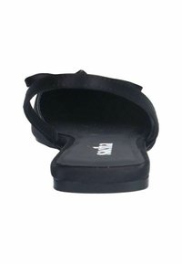 Sandales noires avec une semelle plate, un design de bretelles minimal et une semelle intérieure texturée. L'intérieur présente un logo imprimé en blanc.