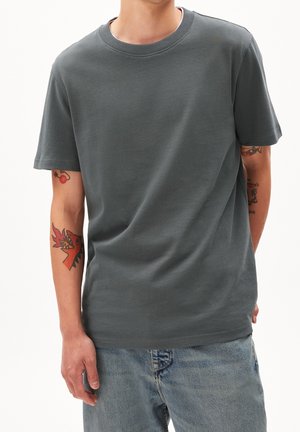 Szary bawełniany t-shirt z klasycznym okrągłym dekoltem, krótkim rękawem i luźnym fasonem. Noszony z jasnoniebieskimi dżinsami.