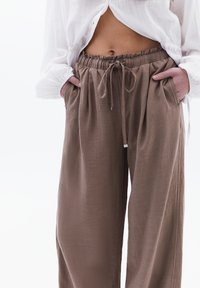 Bruine linnen broek met een elastische tailleband, trekkoordsluiting en zijzakken. Gemêleerde stof met een ontspannen pasvorm en wijde benen.