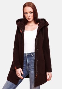 Manteau à capuche marron avec fermeture éclair sur le devant, poches latérales et accents en cuir, porté sur un haut blanc et un jean bleu. Texture de tissu douce.