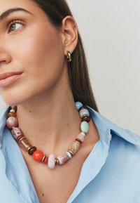 Mehrfarbige Perlenschmuckkette mit verschiedenen Formen und Texturen, darunter pinke, orangefarbene und blaue Steine, ergänzt durch goldene Akzente.