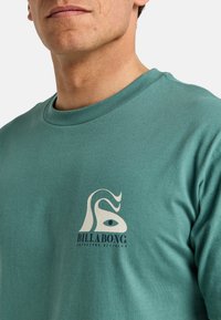 Turquoise katoenen sweatshirt met een wit logo met een golfontwerp en marineblauwe tekst "BILLABONG ADVENTURE DIVISION" op de borst.