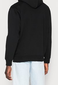 Svart huvtröja med långa ärmar och ribbad nederkant, tillverkad av mjukt tyg. Har en känguruficka fram, enkel design.