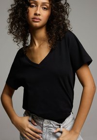 Czarna koszulka V-neck z krótkim rękawem, wykonana z miękkiego materiału. Połączona z jasnoszarymi dżinsami z wysokim stanem. Prosty, czysty design.