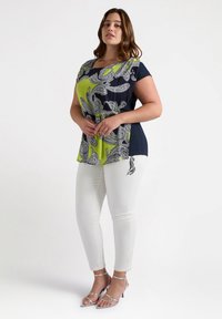 Top de manga corta en azul marino y verde lima con estampado paisley; combinado con pantalones blancos con un diseño sutil; sandalias de tacón plateadas.