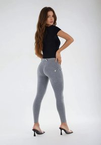 Leggings grises con diseño de costuras curvas, cintura alta y detalle de bolsillo trasero, combinados con una camiseta negra ajustada y sandalias con tacón transparente.
