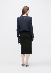 Granatowa bluzka z zakładkami na ramionach, z tyłu z wycięciem w kształcie łezki, zestawiona z dopasowaną czarną spódnicą midi i czarnymi szpiczastymi szpilkami.